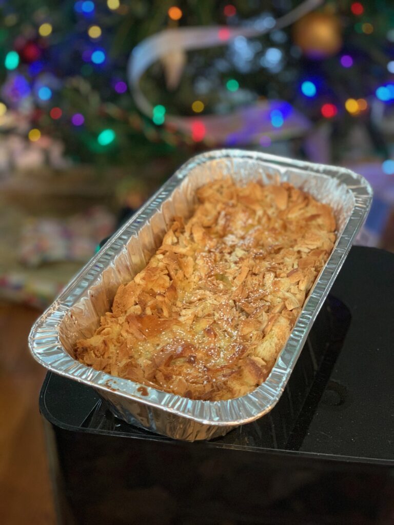 in-focus homemade crème Brulee in foil tin on black surface with decorated and blurred Christmas tree behind it