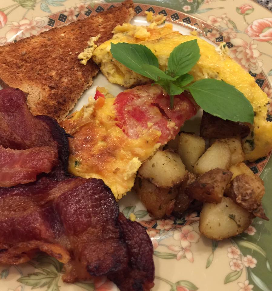 closeup of homemade egg frittata decorated with mint leaves with a side of toast, bacon and hash browns on green china plate with pink flowers