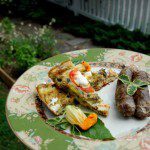 homemade egg frittata decorated with sage leaves with a side of sausage on green china plate with pink flowers with green garden plants in the background and white picket fence