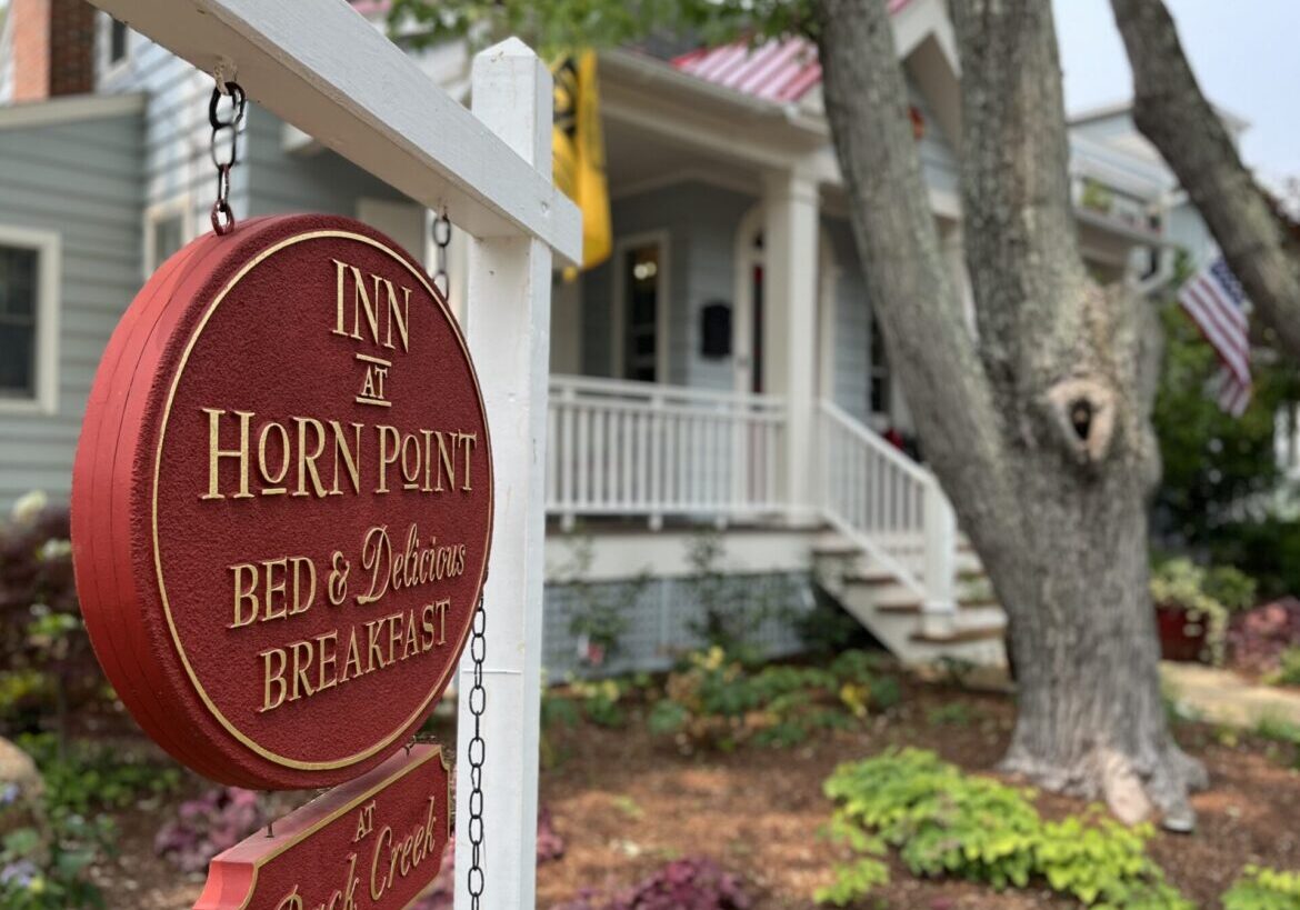 Red and Gold Leaf Bed and Breakfast sign on white post with front porch and entrance in the background