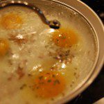 homemade poached eggs on pepperade with organic onions and fresh peppers and smoked salt and black pepper in cast-iron pan with glass lid and silver handle